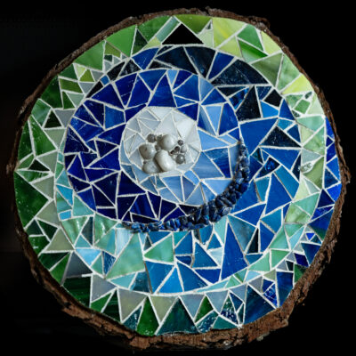 Blue and green glass, stones, and grout on wood